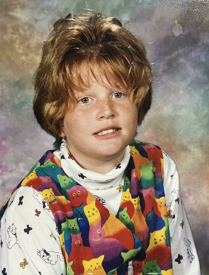Child wearing colorful cat print vest and white turtleneck posing for a hilariously awkward childhood photo.