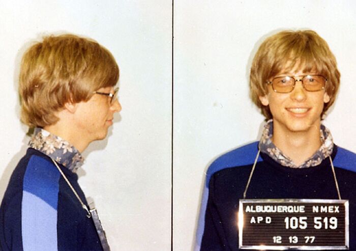 Young male celeb in a mugshot photo wearing glasses and a blue sweater after being arrested in Albuquerque.