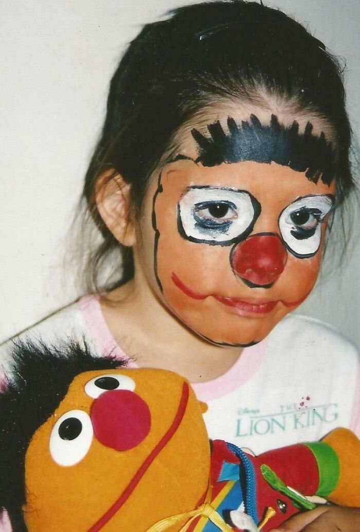 Child with awkward clown face paint holding a puppet, showcasing a hilariously awkward childhood photo moment.
