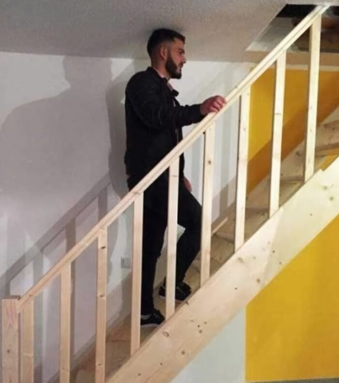 Man using a staircase with poorly constructed railing blocking the stairway, showcasing job done almost impressively wrong.