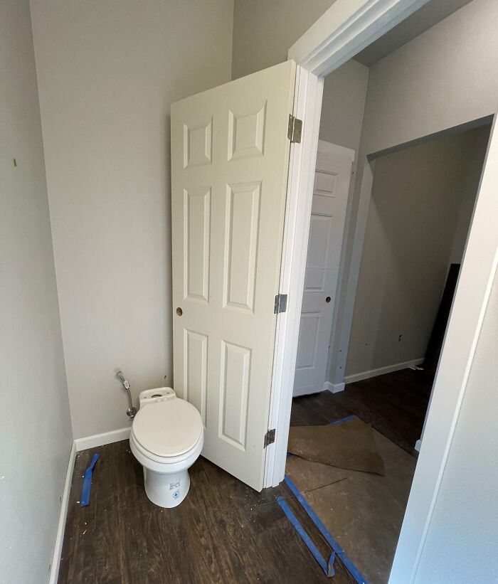 Toilet installed in a small bathroom space blocked by a door, showing an example of poor job e*******n.