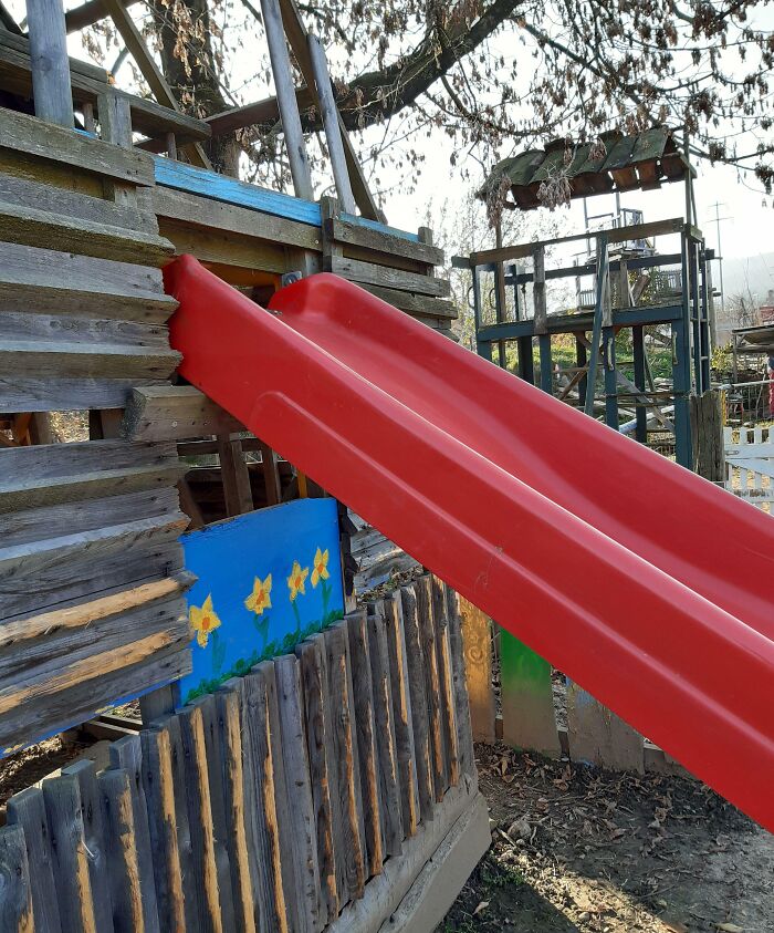 A poorly installed red slide ending abruptly into a wooden fence, showcasing a surprising job failure.