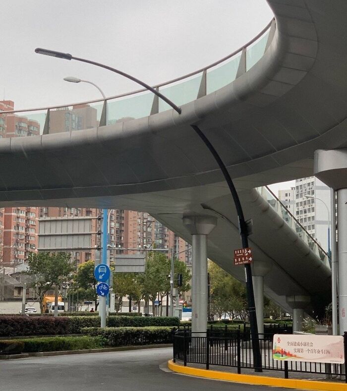 Bent streetlight under overpass showing poor job performance in urban infrastructure and maintenance work.