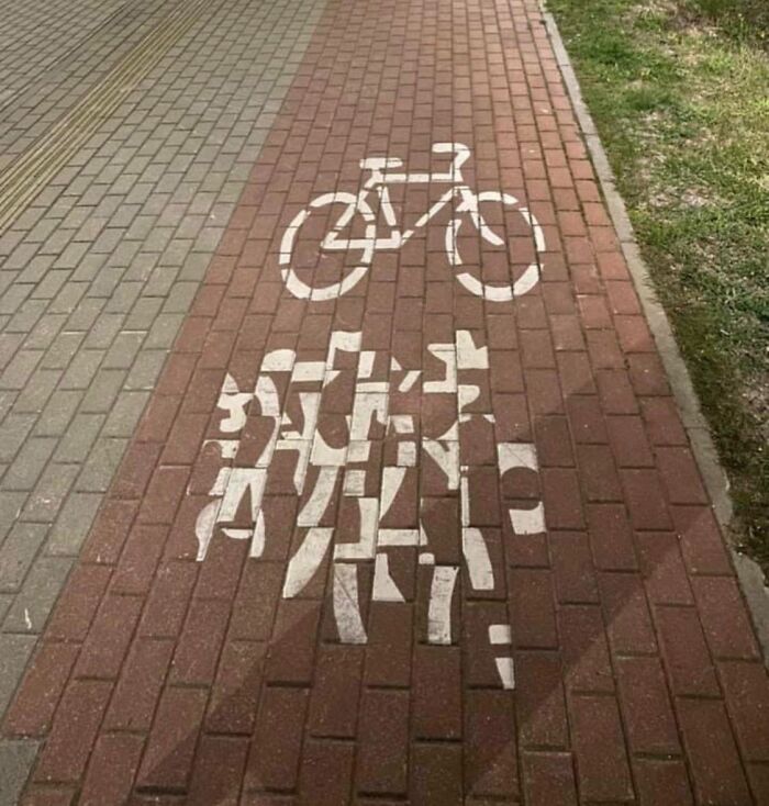 Bike lane marking painted poorly on a brick path with misaligned and distorted white paint job.