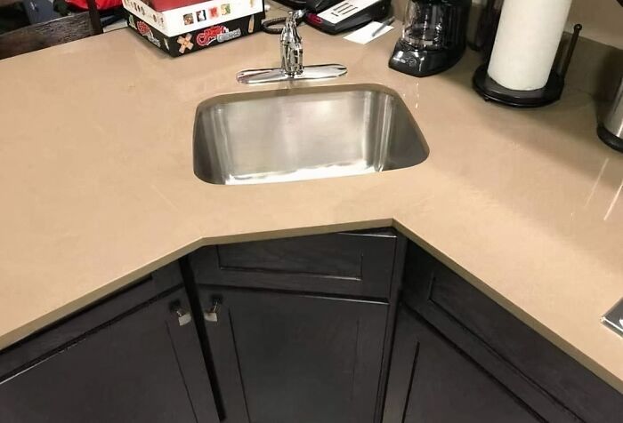 Kitchen sink poorly installed in the corner with an awkward countertop cut, showing a job done almost impressively wrong.