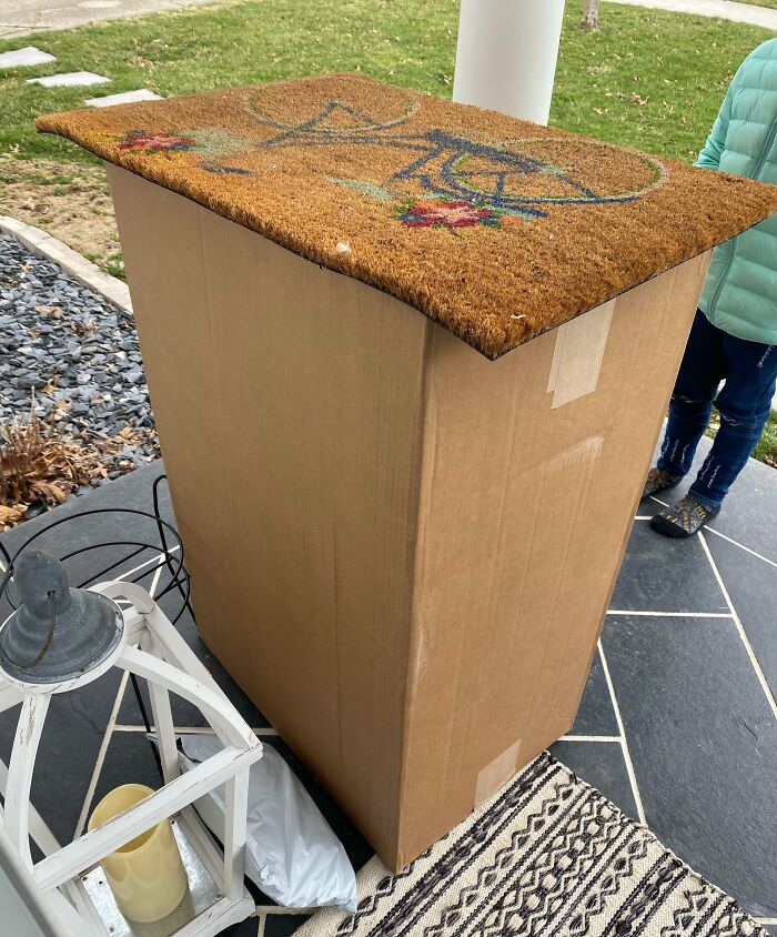 Cardboard box used as a doorstep with a doormat on top, showing a poor job that is almost impressive.
