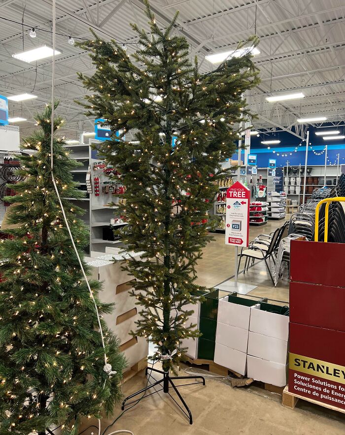 Tall artificial Christmas tree with sparse lights and missing branches displayed in a store, showing poor job e*******n