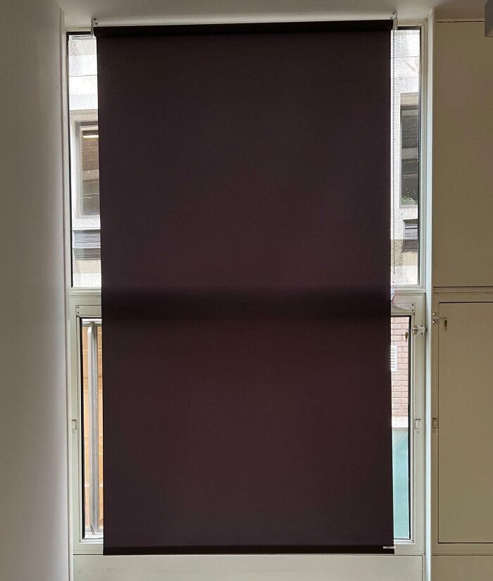 Window with a roller blind installed so poorly that it covers two different window sections unevenly, showing job failure.