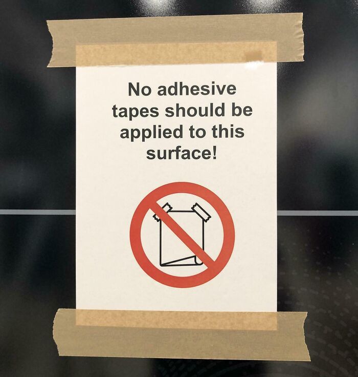 Sign warning against adhesive tapes on surface, ironically taped with adhesive, showcasing poor job e*******n almost impressive.