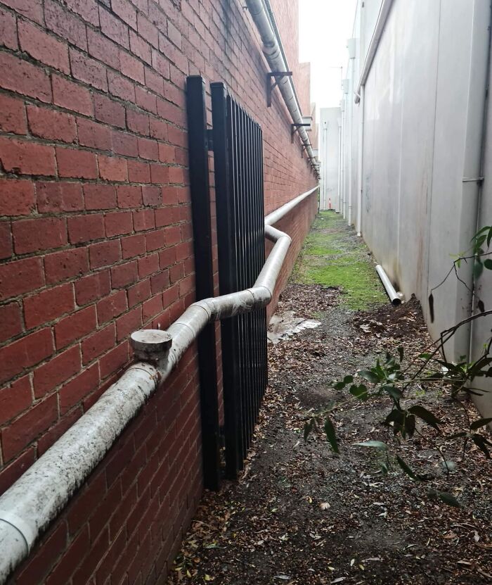 Poorly installed pipe poorly routed through metal bars along a narrow alley showing job fail in construction work.