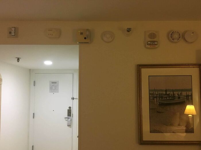 Multiple fire alarms and detectors installed unevenly above a hotel door, showcasing a poor job in safety device placement.