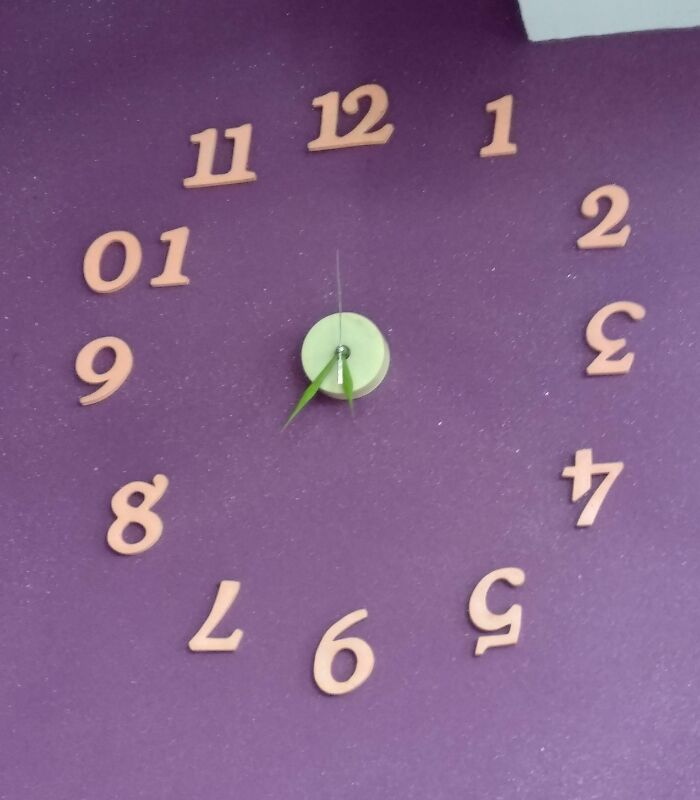 Clock with numbers arranged incorrectly on purple wall, showing a job done so poorly it is almost impressive.