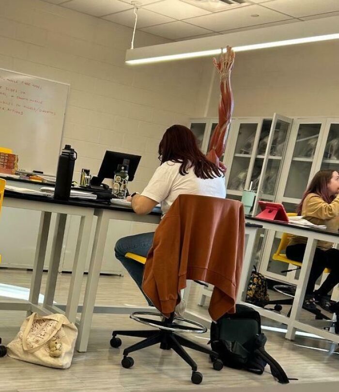 Student sitting in science classroom with arm model aligned oddly behind, creating a confusing visual effect.