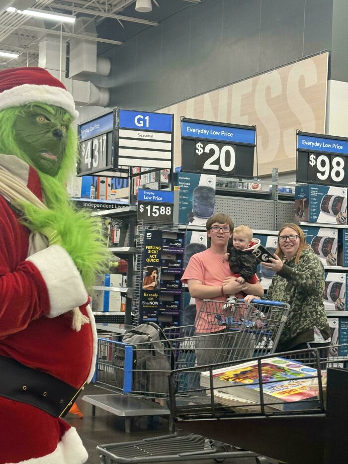 Person dressed as the Grinch in a Walmart store with shoppers and holiday products, capturing unusual Walmart moments.