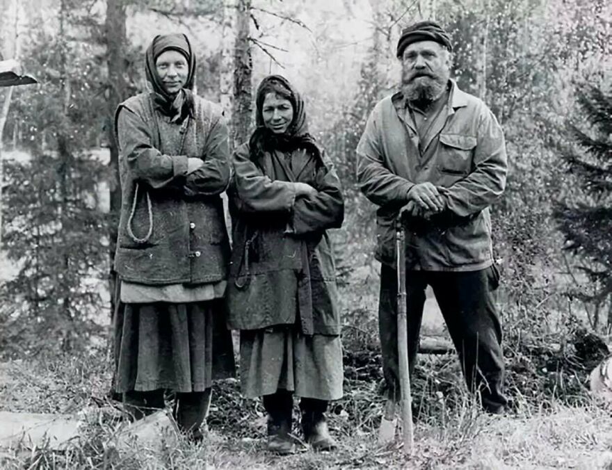 Black and white photo of three people in rustic clothing standing outdoors in a forest, a random picture worth exploring.