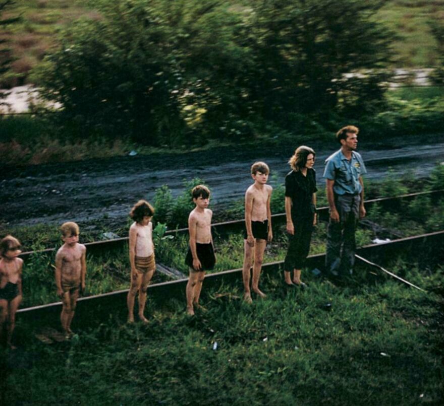 Group of barefoot children and an adult standing in a line outdoors, evoking curiosity in random pictures worth exploring.