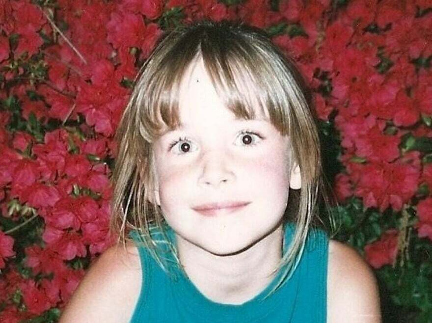 Young girl smiling in front of vibrant red flowers, one of the random pictures people say are worth exploring.