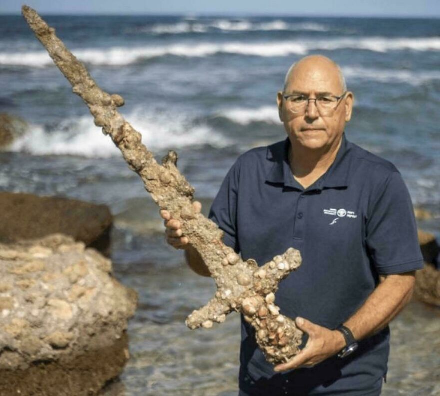 Man holding barnacle-covered sword by the ocean, one of the random pictures people say are worth exploring.