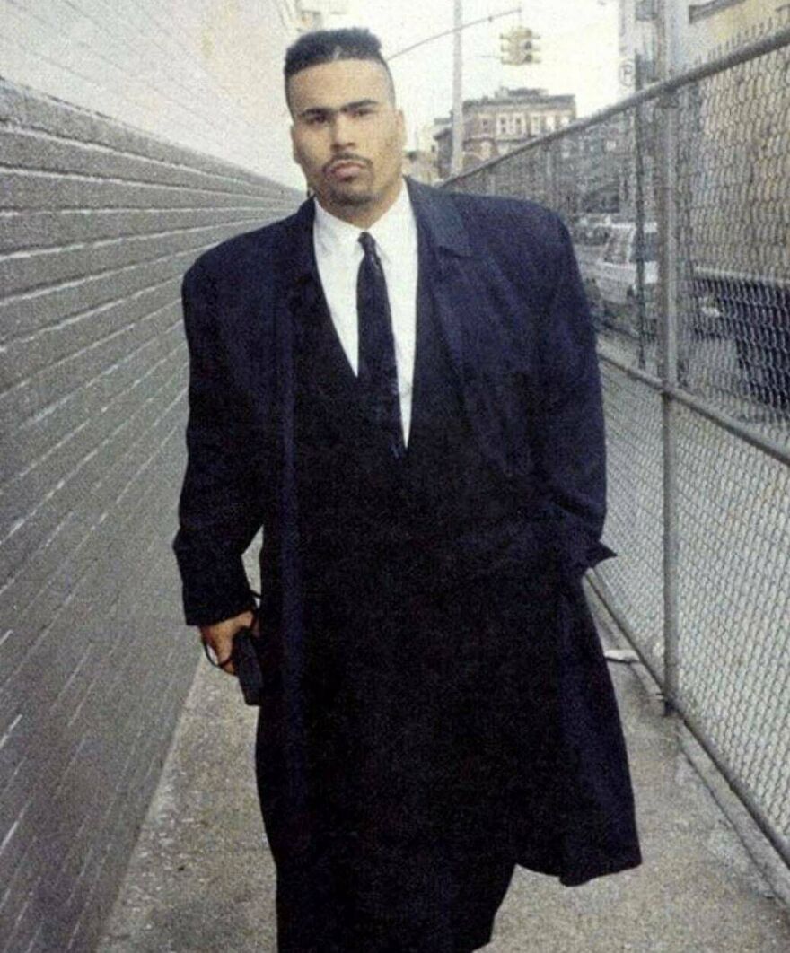 Man wearing an oversized black suit walking down a narrow urban alley, a unique random picture worth exploring.