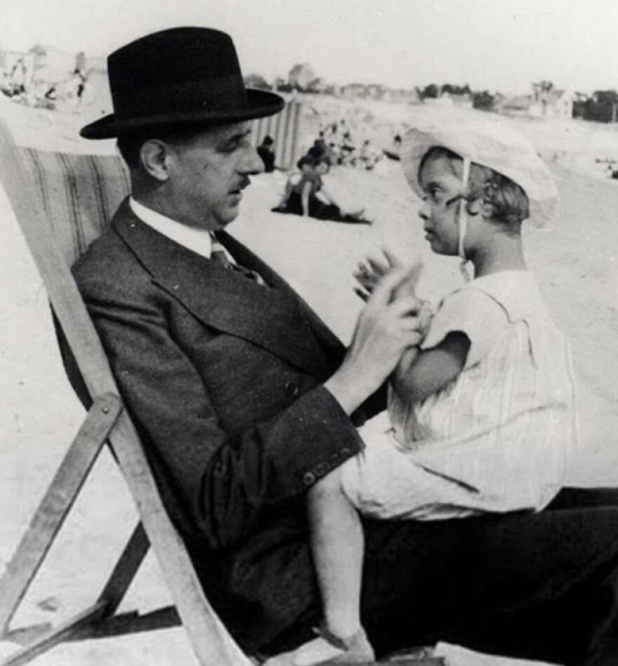 Black and white photo of a man in a hat and suit playing with a young child on a beach, random pictures concept.