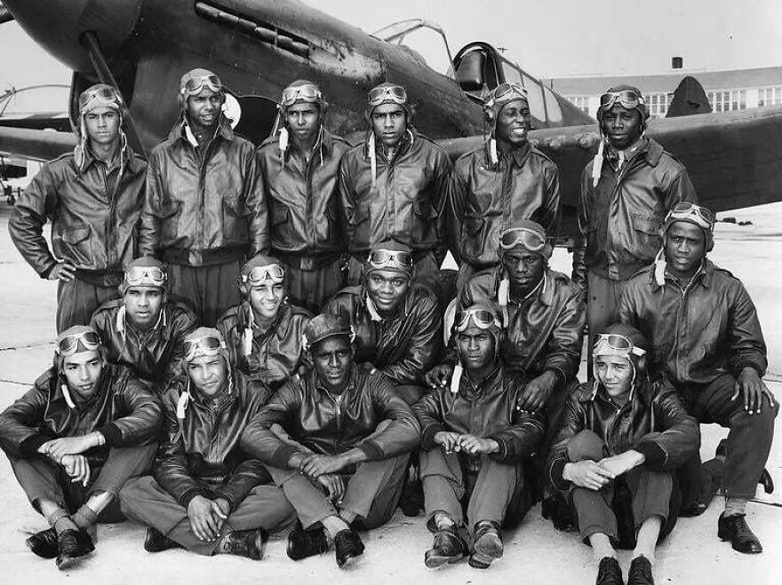 Group of WWII pilots in leather jackets and goggles posing in front of airplane, a fascinating random picture to explore.