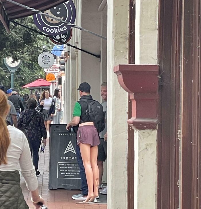 Man wearing shorts that appear like a short skirt gives a confusing visual in a busy street photo to challenge your brain.