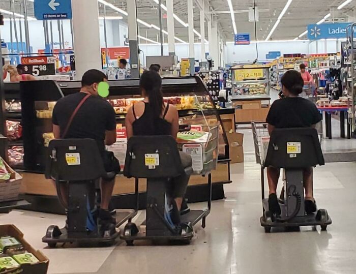 Three people riding motorized shopping scooters side by side in a Walmart store aisle with various products around.