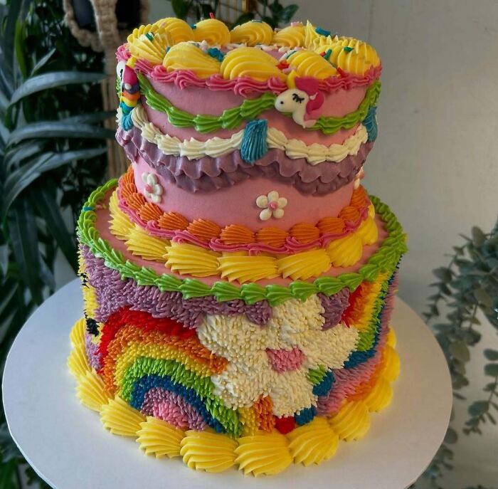 Colorful masterfully crafted cake decorated with rainbows, flowers, and a unicorn, showcasing human creativity in cake design.