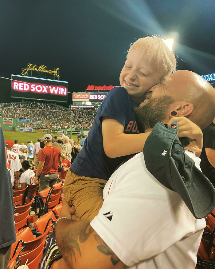Father and son sharing a heartwarming hug at a baseball game celebrating a Red Sox win with joyful smiles.