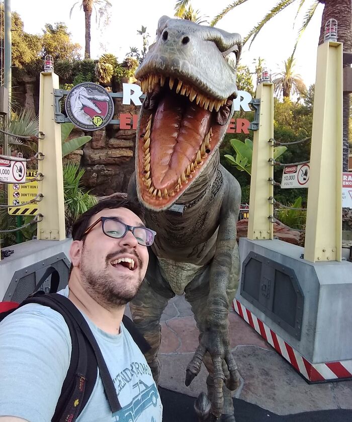 Man taking a selfie next to a lifelike T-Rex dinosaur statue, symbolizing a leap of faith and bold life decisions.