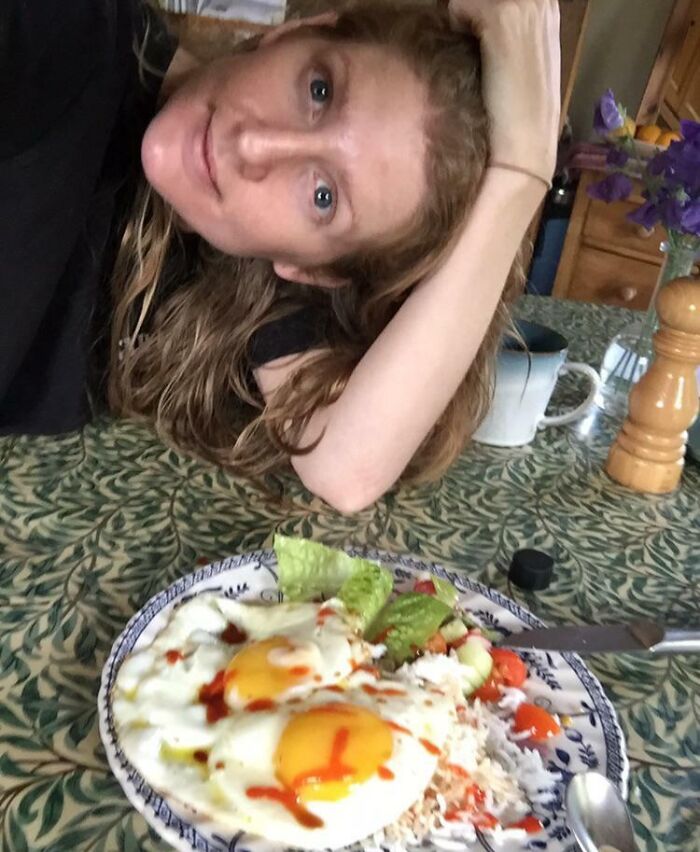 Woman with long hair resting head on hand at table with breakfast plate showing eggs over rice and vegetables in leap of faith moment