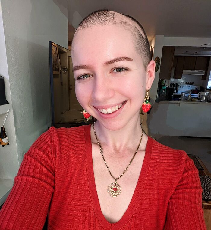 Smiling person with shaved head wearing red top and strawberry earrings, representing leap of faith and best life decisions.