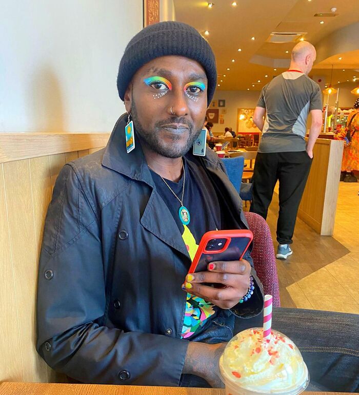 Person with colorful makeup and earrings sitting in a cafe, holding a phone, representing leap of faith decisions.