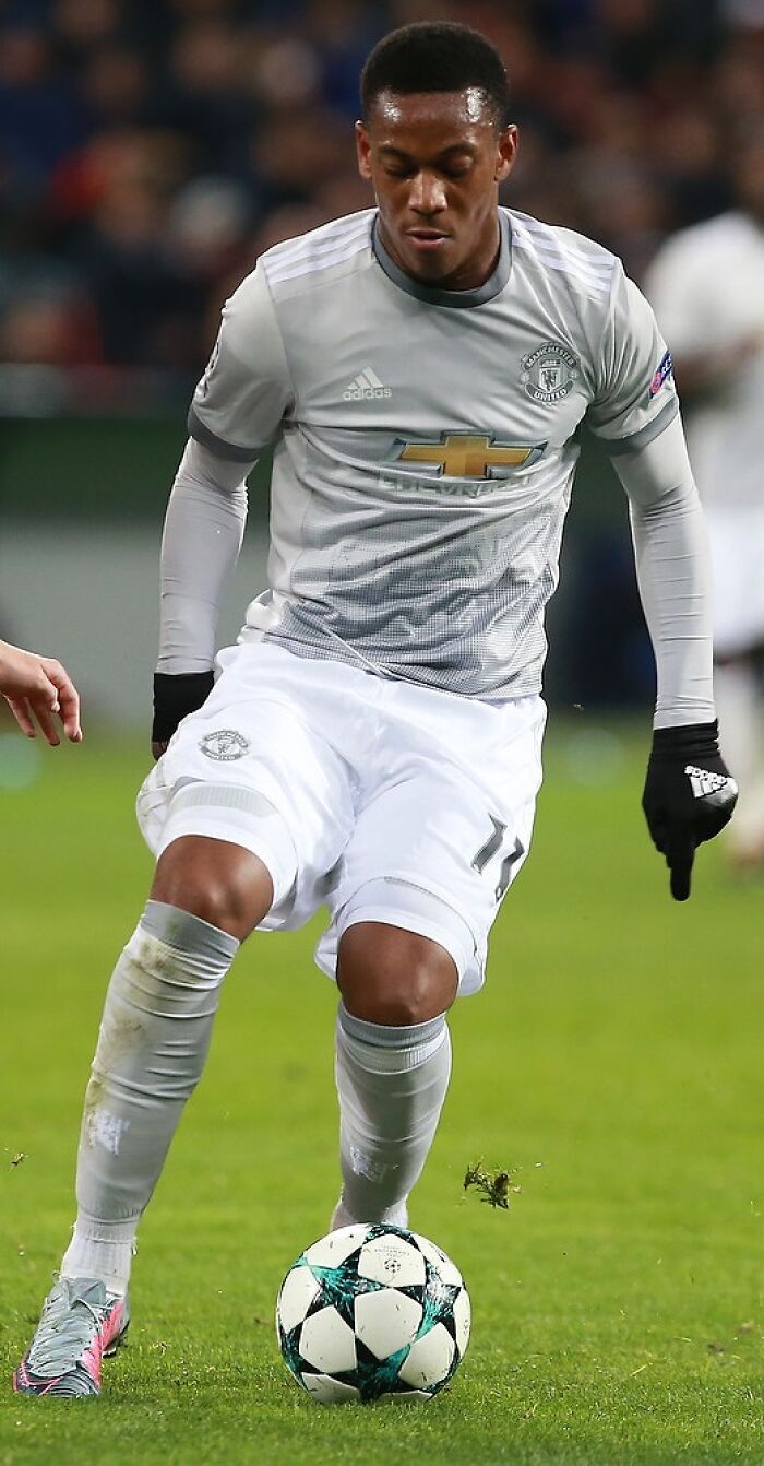 Anthony Martial controlling a soccer ball during a match in a Manchester United away kit on the field.