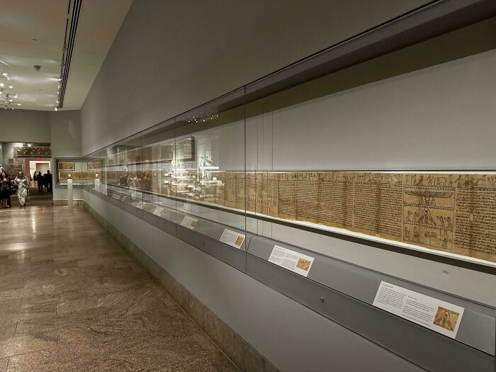 Ancient Egypt museum exhibit showcasing long papyrus scroll with hieroglyphics behind glass in well-lit gallery space.