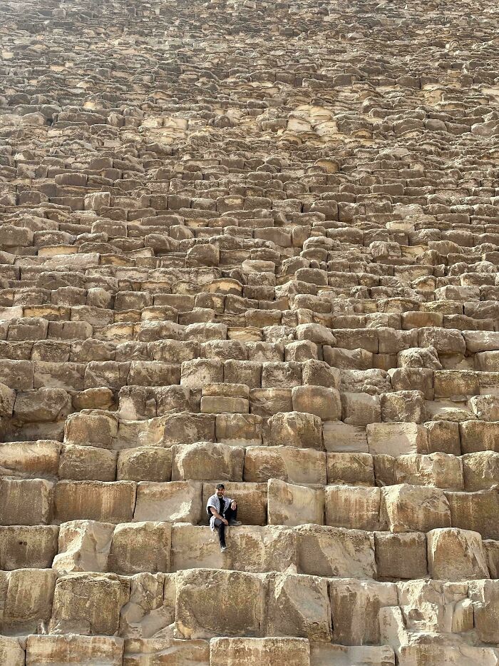 Person sitting on large ancient stones of a pyramid wall, showcasing incredible photographs from Ancient Egypt history.