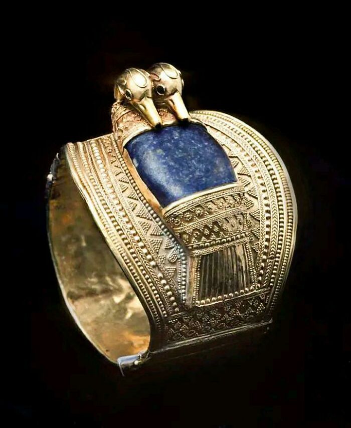 Ancient Egypt gold bracelet with intricate patterns and blue stone centerpiece featuring two bird heads design on black background
