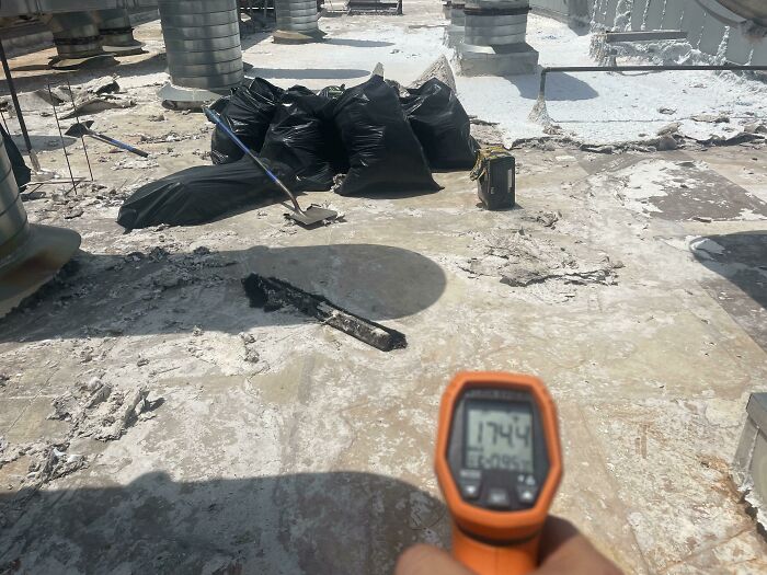 Infrared thermometer held on a rooftop with construction debris and black trash bags in the background, showcasing different jobs.