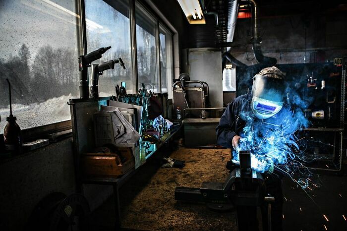 Welder in protective gear creating sparks, showcasing a fascinating job that makes the 9-to-5 workday more bearable.