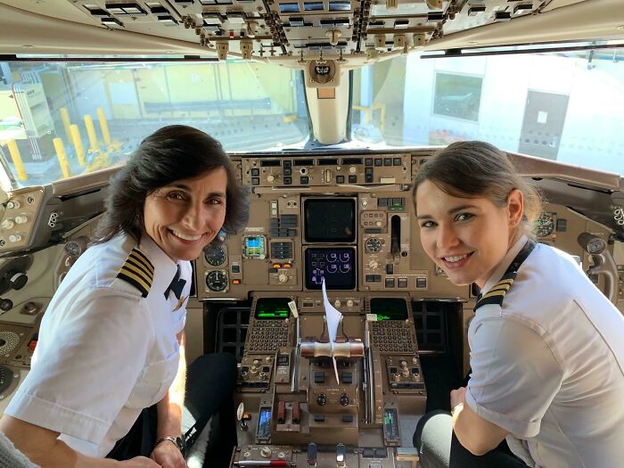 Two female pilots smiling inside a commercial airplane cockpit showcasing fascinating jobs that brighten a 9-to-5 workday.
