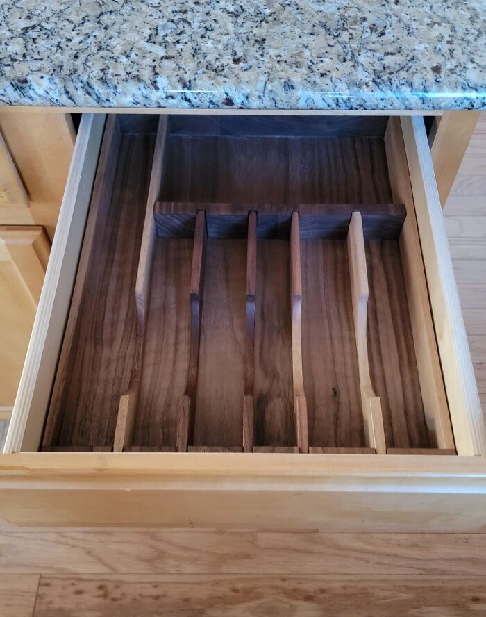 Woodworkers crafted a custom wooden drawer organizer with multiple compartments beneath a granite countertop.