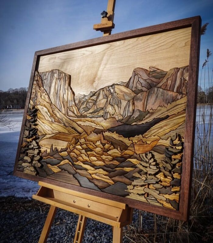 Intricate wooden landscape carving showcasing detailed mountains and trees, a standout woodworking project outdoors on an easel.