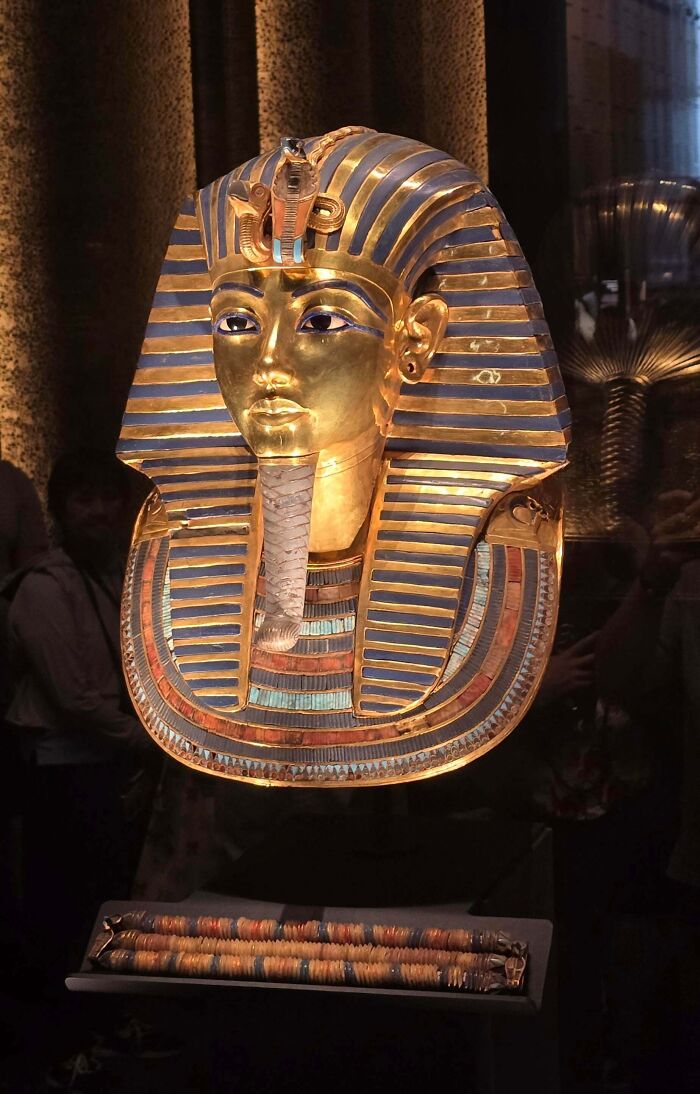 Ancient Egypt golden funerary mask with detailed blue and gold stripes displayed in a museum setting.