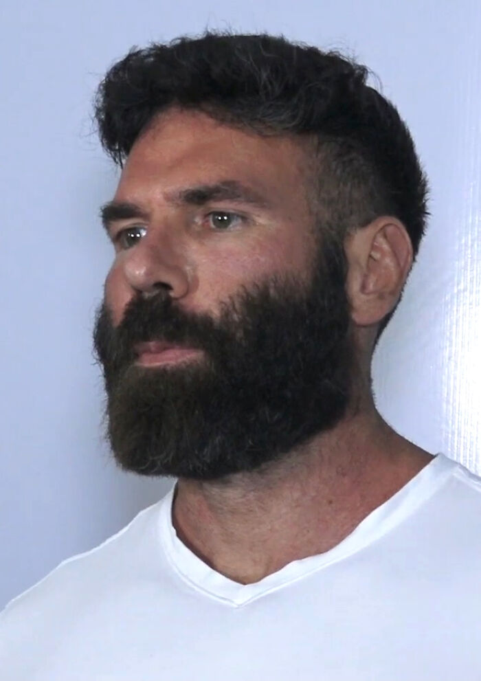 Dan Bilzerian with a thick beard and short hair wearing a white shirt against a plain background.