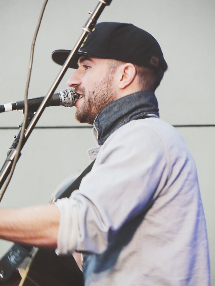 Sam Hunt performing live on stage, singing into a microphone while playing guitar during a music event.