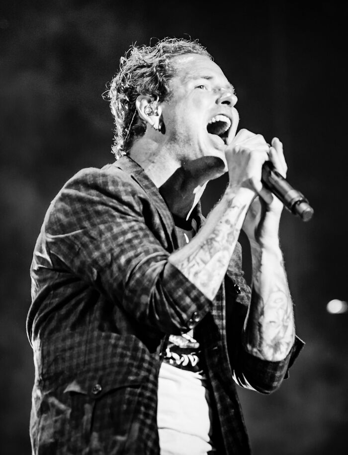 Corey Taylor performing live on stage, holding a microphone and passionately singing during a concert.