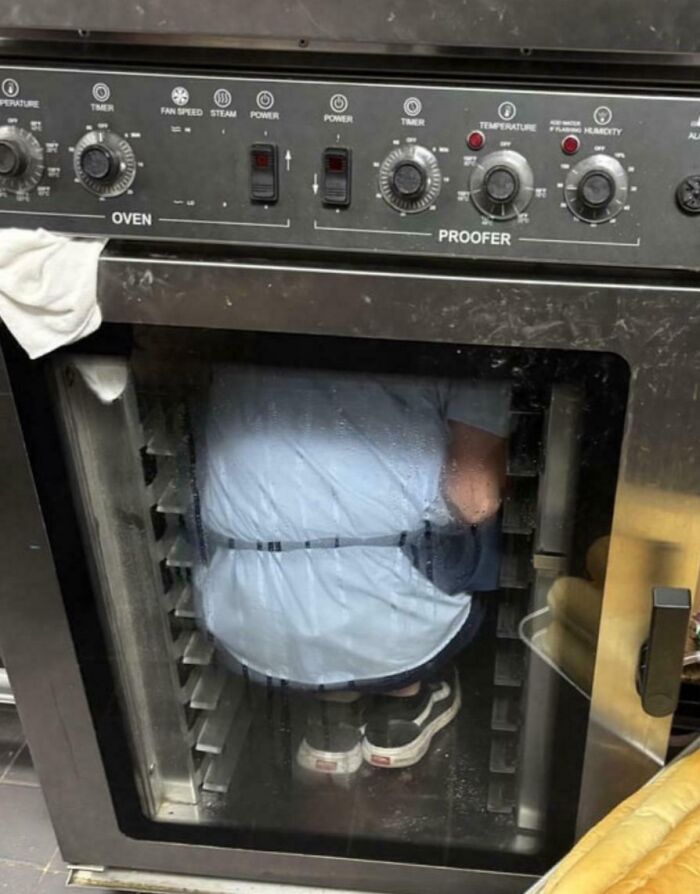 Employee blatantly ignoring safety protocol by climbing inside a commercial oven, making an extremely dangerous decision.