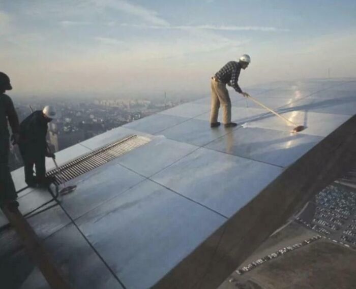 Workers blatantly ignored safety protocol while working at extreme heights on a steep metal rooftop without proper protection.