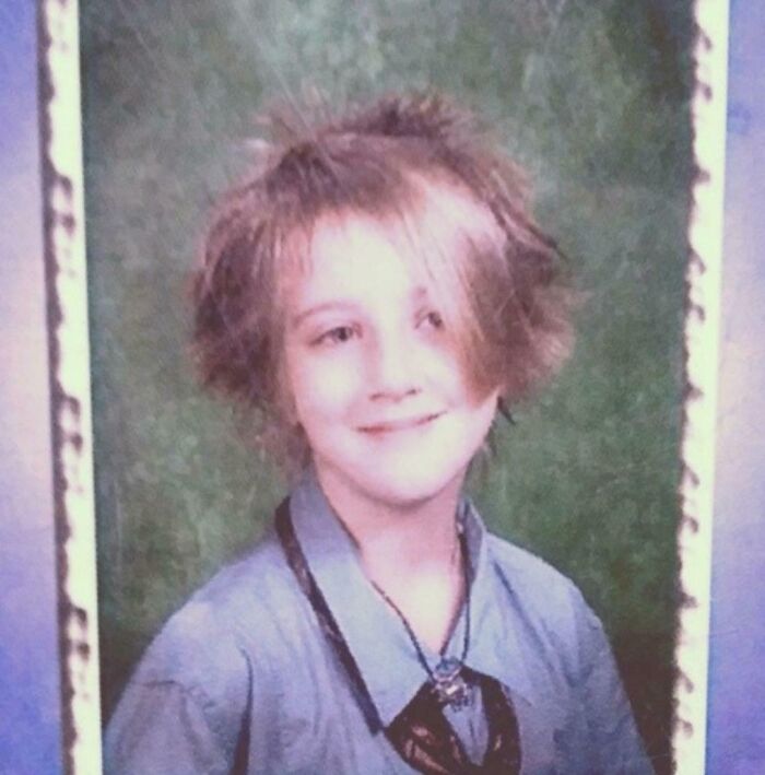 Awkward childhood photo of smiling boy with messy hair and loose tie against a green school photo background.