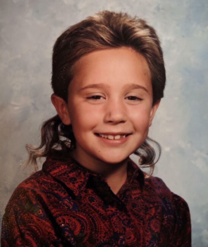 Smiling young boy with a mullet hairstyle wearing a patterned shirt in a hilariously awkward childhood photo.